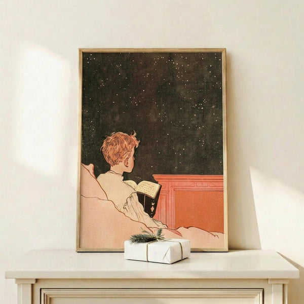 May include: Vintage-style poster in thin wooden frame showing person with reddish hair in cream clothing reading book while gazing at starry night sky, displayed on light wood surface next to small white wrapped gift with greenery sprig against cream wall