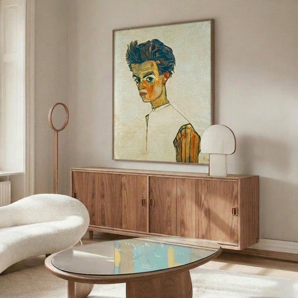 May include: Expressionist self-portrait artwork displayed above wood sideboard in modern living room setting. The painting shows a young man with dark tousled hair and angular features in white shirt, rendered in bold blues, oranges and yellows against cream background. Warm walnut furniture, white curved chair, glass coffee table, and soft natural lighting complete the contemporary interior scene.