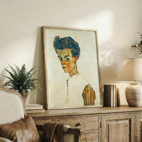 May include: Framed reproduction of an early 20th century self-portrait showing a young man with tousled dark hair and intense gaze, painted in expressive style with bold brushstrokes in blues, oranges and yellows against cream background. Wooden frame displayed on rustic sideboard with fern plant, ceramic vases, and books in neutral-toned living room setting.