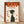 May include: Framed poster print leaning against white wall on light wooden floor. The artwork features a minimalist design with rust-orange border and cream background. A woman's profile silhouette in dark green faces right, with geometric orange squares scattered around. Large "ZEN" text at top, Japanese characters below including "背中に空気を感じる" and other text elements. Natural wood frame with warm lighting casting soft shadows on textured wall.