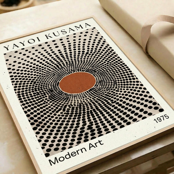May include: Framed art print featuring a radiating pattern of black dots creating an optical illusion with an orange-brown circle at the center, displayed on a cream colored surface next to rolled white paper. The vintage-style poster shows "YAYOI KUSAMA" at the top, "Modern Art" at the bottom, and "1975" in the corner, with dots arranged in concentric circles that appear to pulse outward from the central orange focal point.