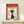 May include: Framed poster with vintage-inspired design featuring profile silhouette of woman with dark hair against cream background, large orange "ZEN" text at top, Japanese characters scattered throughout, rust-orange border, displayed on light wood surface next to small white wrapped gift with greenery sprig, against neutral wall with natural lighting