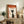 May include: Framed poster with Japanese text and silhouette of person in profile, displayed on rustic wooden console alongside fern plant, ceramic vases, and books in neutral-toned living room setting. Orange and cream color scheme with geometric design elements.