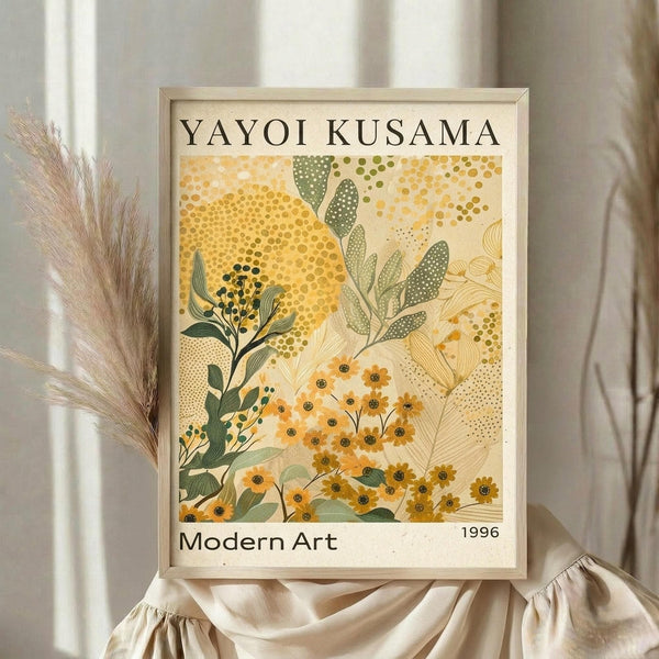 May include: A framed art print featuring botanical illustrations in yellow and green tones with dotted patterns and abstract floral motifs, displayed on a beige fabric backdrop with dried pampas grass stems visible to the left. The artwork shows stylized plants and flowers with polka dot textures in an organic, modern style within a light wood frame.