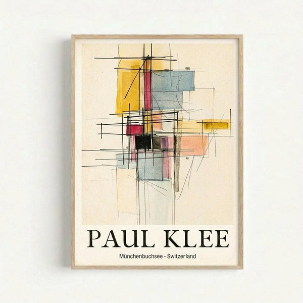 Framed abstract geometric artwork featuring overlapping rectangles and squares in yellow, red, blue, pink, and black with intersecting black lines on cream background. The composition has an architectural, grid-like structure with transparent color blocks creating depth. Text below reads "PAUL KLEE" and "Münchenbuchsee - Switzerland" in black serif font. Light wood frame against white wall.