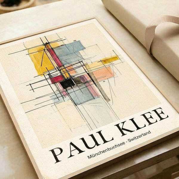 May include: Abstract geometric artwork poster featuring intersecting black lines with colorful rectangular shapes in yellow, red, blue, and pink watercolor-style blocks. The minimalist print sits on a cream-colored surface next to rolled paper tubes, displaying the artist's name and Swiss location in black text below the composition.