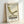 May include: Framed vintage-style poster featuring a minimalist green lounge chair illustration with curved X-frame base, displayed in natural wood frame against white wall. Cream background with retro typography reading "1983," "Timeless Design," and "VISIONS" in brown text. Mid-century modern aesthetic with clean lines and muted olive green upholstery details.