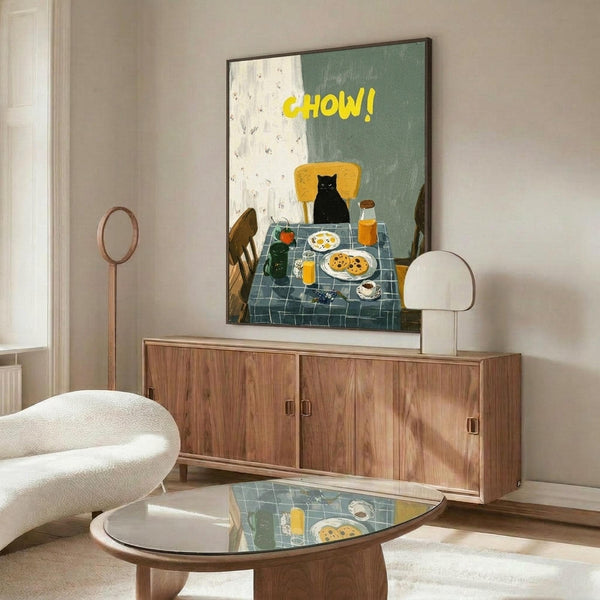 May include: Framed poster displaying a black cat sitting at breakfast table with yellow "CHOW!" text, shown in modern living room with walnut credenza, white curved chair, glass coffee table, and warm lighting. Art features checkered tablecloth, eggs, pancakes, and orange juice in folk art style with sage green and cream background.