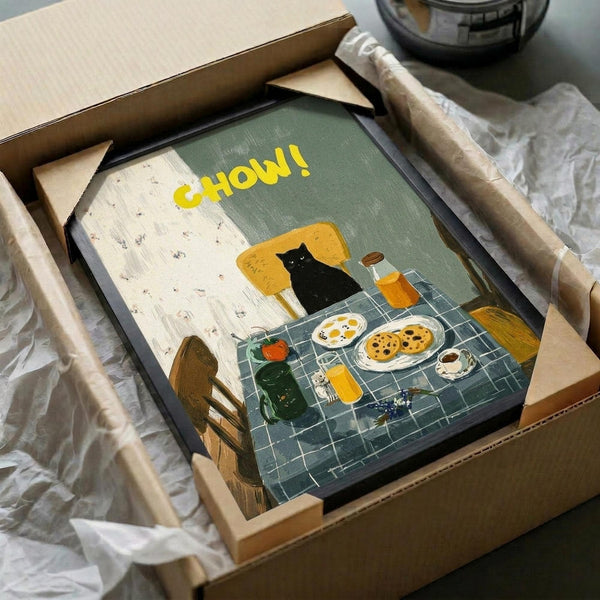 May include: Framed art print in cardboard shipping box with protective wrapping. Illustration shows black cat sitting in yellow chair at blue checkered table with breakfast items - plates of eggs and cookies, coffee cup, orange juice. Yellow "CHOW!" text at top. Cozy kitchen scene with floral wallpaper background in warm, vintage-inspired art style.