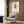 May include: Abstract geometric artwork poster with colorful overlapping rectangles in yellow, red, blue, and orange connected by black lines, displayed in light wood frame on textured wood paneled wall. Modern beige armchair with geometric patterned pillow sits below artwork, alongside brass floor lamp and dark round side table with open book.