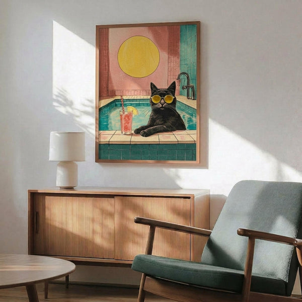 May include: Framed poster print hanging above wooden credenza showing black cat wearing yellow sunglasses lounging by turquoise swimming pool with coral drink nearby, bright yellow sun in coral sky background, displayed in modern living room with mint green mid-century chair and white ceramic lamp