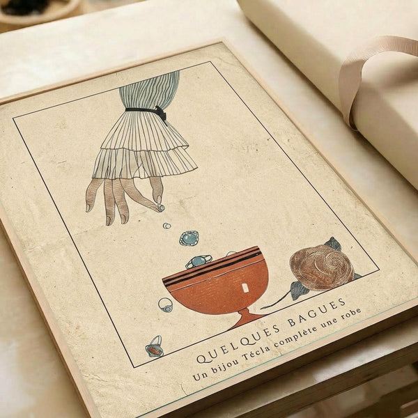 May include: Vintage-style Art Deco poster print displayed in an open book or portfolio with cream-colored pages and beige ribbon binding. The illustration features a woman's lower body in a striped dress and stockings reaching toward an ornate orange teacup, with decorative swirls and geometric elements. The artwork has muted teal, orange, and brown colors on aged paper texture with French text at the bottom.