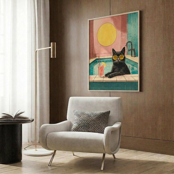 May include: Framed poster print featuring a black cat wearing yellow sunglasses lounging by a turquoise swimming pool with a tropical drink, yellow sun and coral-pink sky in background. Modern living room setting with beige armchair, geometric pillow, brass floor lamp, and wood-paneled wall. Warm natural lighting through window curtains.