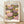 May include: Framed poster print featuring pink and purple lotus flowers with olive green lily pads on dark background, displayed in light wood frame leaning against white wall on wooden floor with soft natural lighting and shadows