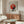 May include: Framed Bauhaus exhibition poster with geometric red, black, and gray circular design hanging above wooden sideboard in modern living room. White sculptural chair and glass coffee table with colorful abstract art visible. Minimalist interior with neutral walls and natural lighting.