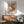 May include: Framed art print featuring colorful water lilies and lily pads in pink, purple, yellow and green tones, displayed above a wooden sideboard in a modern living room with mint green upholstered chair, white table lamp, and natural sunlight casting shadows on white walls.