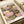 May include: Framed art print featuring pink and purple flowers with green leaves on dark background, displayed on light wooden surface next to cream colored ribbon. The vintage-style floral artwork shows soft pastel blooms in an impressionistic pattern with dotted textures throughout the design.