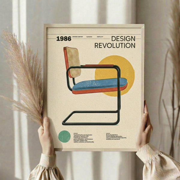 May include: Person holding framed vintage-style poster featuring modernist cantilever chair with woven cane back, colorful striped seat cushion in blue and coral, black tubular frame, yellow circle backdrop. Text reads "1986 Design Revolution" with small descriptive paragraphs below. Light wood frame, cream background, dried pampas grass visible, neutral beige clothing and curtained window setting.