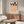 May include: Framed vintage-style poster featuring three women in pink and yellow clothing with black silhouettes behind them, displayed above a walnut wood credenza in a modern living room with cream walls, white upholstered chair, glass coffee table, and warm natural lighting creating reflections on the floor.
