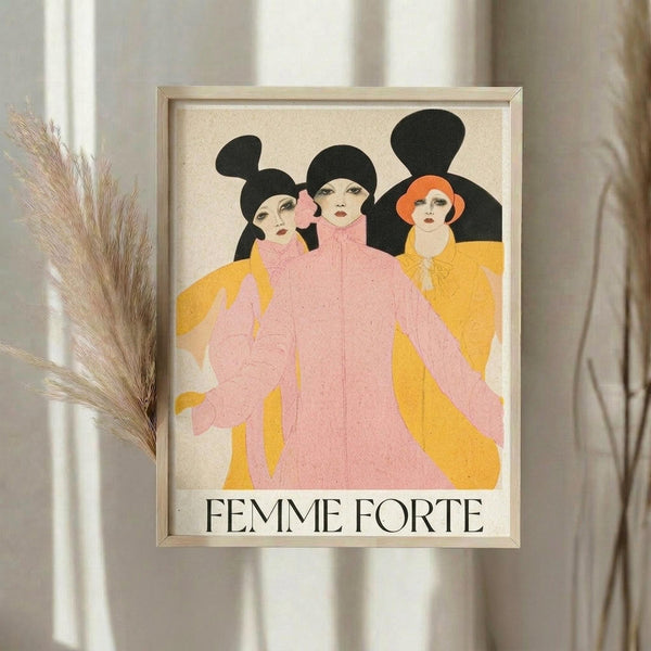 May include: Framed poster featuring three women in Art Deco style illustration with black hair, pink and yellow flowing garments, and "FEMME FORTE" text below. Light wood frame displayed on white wall beside dried pampas grass in neutral home setting with soft natural lighting.