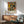 May include: Paul Klee abstract art print in wooden frame hanging above mid-century modern credenza with white ceramic lamp. Print features colorful geometric shapes in yellow, orange, red, and black arranged in grid pattern. Modern living room setting with teal upholstered armchair, round wooden coffee table, white walls with natural sunlight streaming across the space.
