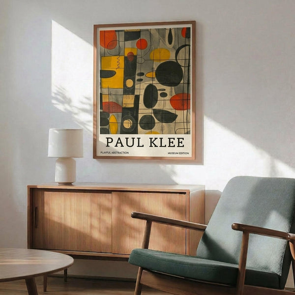 May include: Paul Klee abstract art print in wooden frame hanging above mid-century modern credenza with white ceramic lamp. Print features colorful geometric shapes in yellow, orange, red, and black arranged in grid pattern. Modern living room setting with teal upholstered armchair, round wooden coffee table, white walls with natural sunlight streaming across the space.