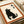 A black cat sits looking upward with Japanese kanji characters above it on cream-colored textured paper. The minimalist artwork features a silhouetted cat with white paws and whiskers, framed by a rust-colored border. The print appears to be displayed on white paper or canvas material with rolled edges visible in the background.