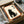 May include: Black cat artwork print in wooden frame with orange mat, displayed in gift box with tissue paper. Japanese characters appear above stylized black cat silhouette on cream background. Frame sits among wooden rolling pins and packaging materials on white surface.