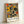 May include: Framed abstract art print leaning against white wall, featuring geometric shapes in yellow, orange, red, and dark green with curved lines and circular forms. Light wood frame surrounds the artwork with white matting. Text at bottom reads "PAUL KLEE" and "PLAYFUL ABSTRACTION MUSEUM EDITION" in black letters.