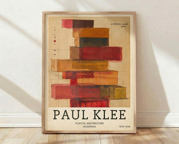 May include: Framed poster print featuring abstract geometric composition with overlapping translucent rectangular blocks in warm colors including reds, oranges, yellows, and browns arranged vertically on cream background. Text reads "architectural poem" at top, "PAUL KLEE" in large black letters, "PLAYFUL ABSTRACTION MODERNISM" below, and "1879-1940" at bottom right. Light wood frame sits against white wall on wooden floor with natural shadows.