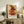 May include: Framed Paul Klee art print displayed on rustic wooden sideboard in warm living room setting. Abstract geometric composition features stacked colorful rectangular blocks in reds, oranges, yellows and browns on cream background with grid lines. Styled with fern plant, pottery vase, books, and brown leather chair visible. Natural lighting creates cozy atmosphere.