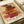 May include: Abstract geometric art print featuring overlapping rectangular blocks in warm earth tones - reds, oranges, browns, and yellows arranged in horizontal layers. The poster displays "PAUL KLEE" and "PLAYFUL ABSTRACTION MODERNISM 1879-194" text at bottom. Print appears mounted or framed, photographed on white paper with rolled paper tubes visible in background, creating an artistic workspace setting.