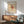 May include: Paul Klee modernist artwork poster displayed in mid-century modern living room with geometric abstract design featuring triangular and circular shapes in black, red, and beige tones. Framed print hangs above wooden sideboard with white ceramic lamp, next to sage green upholstered armchair with walnut frame and small round coffee table on hardwood floors.