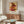 May include: A framed poster featuring colorful abstract geometric blocks in red, orange, and green tones on cream background, displayed on a wooden sideboard in a modern living room with white curved chair, glass coffee table, and contemporary lighting fixtures.
