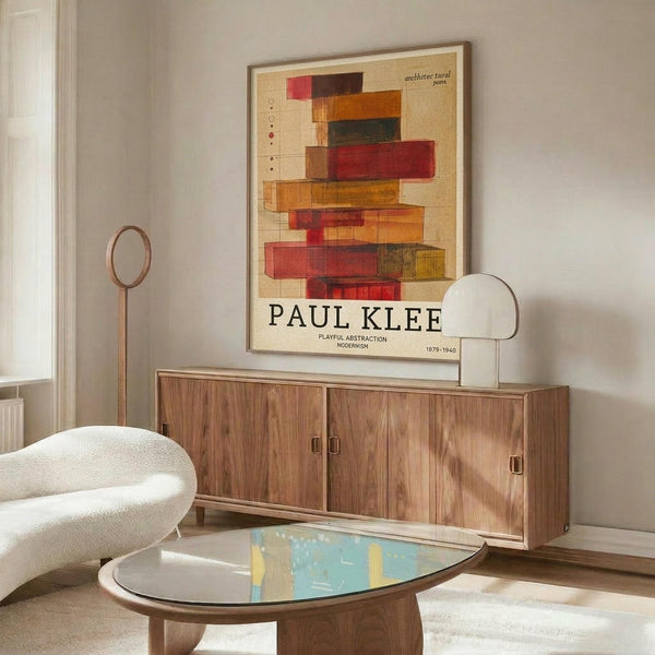 May include: A framed poster featuring colorful abstract geometric blocks in red, orange, and green tones on cream background, displayed on a wooden sideboard in a modern living room with white curved chair, glass coffee table, and contemporary lighting fixtures.