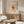 May include: Paul Klee modernist art print in light wood frame hanging above walnut sideboard in bright living room. Abstract artwork features geometric shapes, lines and warm earth tones on cream background. White curved chair and oval glass coffee table with colorful surface visible in foreground. Modern floor lamp with circular shade stands beside sideboard.