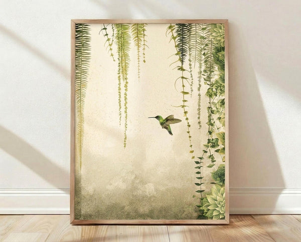 May include: Framed botanical wall art print featuring a small green hummingbird in flight surrounded by cascading ferns and trailing vines on a cream textured background. The artwork is displayed in a light wood frame, leaning against a white wall on light wooden flooring with natural shadows cast across the scene.