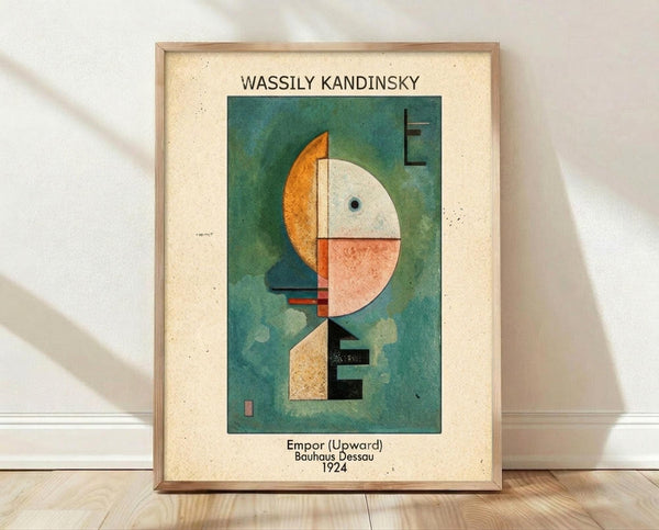 May include: Framed abstract art print leaning against white wall on light wood floor. Cream matted poster features geometric composition with orange crescent, white and coral semicircles, black rectangular forms on teal-green background. Text identifies artist, artwork title, and 1924 date. Natural lighting creates soft shadows on textured white wall.