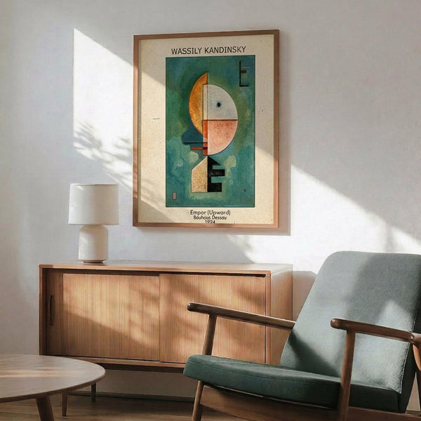 May include: Framed Kandinsky abstract art print hanging above wooden sideboard in modern living room. Poster features geometric shapes in green, orange, white and pink tones. Mid-century furniture includes teal upholstered armchair with wooden frame, walnut credenza with sliding doors, white ceramic table lamp, and round coffee table. Natural sunlight creates shadows on white walls.