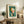 May include: Framed Kandinsky abstract art print featuring geometric shapes in teal, orange, white and pink on cream mat, displayed on rustic wooden sideboard with fern plant, ceramic vase, books, and brown leather chair visible in cozy living room setting