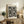 May include: Framed black and white polka dot art print leaning against white wall on rustic wooden sideboard. Print features dense pattern of various sized black circles and dots on cream background. Scene includes beige upholstered chair, potted fern, stacked books, ceramic vase, and warm natural lighting creating cozy living room atmosphere.