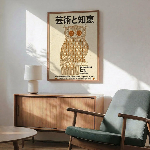 May include: Framed vintage Japanese poster featuring geometric owl illustration in warm brown tones, displayed above mid-century modern walnut credenza with white ceramic lamp. Green upholstered armchair with wooden frame sits nearby on light wood floor, with dramatic window shadows creating triangular light patterns on white wall.