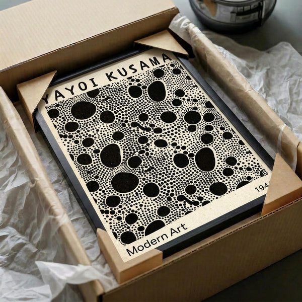 May include: Framed art print featuring black polka dots of varying sizes on cream background, displayed in thin black frame inside open cardboard shipping box with protective tissue paper wrapping