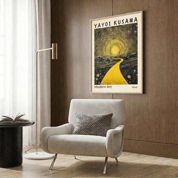 May include: Framed poster featuring yellow sun with radiating dotted pattern and bright yellow path against dark starry background, displayed on wood paneled wall above beige upholstered armchair with geometric patterned pillow, brass floor lamp and side table with open book nearby