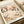 May include: Art print featuring delicate cherry blossom branches with pink and white flowers against a cream background, displayed in a light wood frame on white paper with beige ribbon nearby. The botanical illustration shows flowing black dotted branches with soft floral details in muted tones.