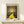 May include: Framed art poster displayed on light wood shelf against cream wall, featuring yellow winding path leading to bright sun with dotted starry sky in Kusama's signature polka dot style. Small white wrapped gift with evergreen sprig sits beside the wooden-framed print. Artwork shows cosmic landscape with flowing hills in dark blues and greens, golden sun rays, and scattered colorful dots throughout the composition.