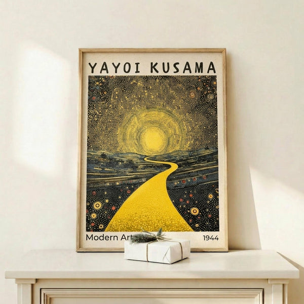May include: Framed art poster displayed on light wood shelf against cream wall, featuring yellow winding path leading to bright sun with dotted starry sky in Kusama's signature polka dot style. Small white wrapped gift with evergreen sprig sits beside the wooden-framed print. Artwork shows cosmic landscape with flowing hills in dark blues and greens, golden sun rays, and scattered colorful dots throughout the composition.
