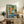 May include: Framed abstract geometric art print displayed on rustic wooden sideboard in modern living room setting. Artwork features colorful collage-style composition with turquoise, orange, green blocks, vintage turntable illustration, and French text at bottom. Styled with fern plant, ceramic vase, books, and neutral furniture.