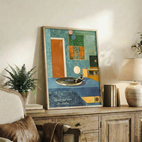 May include: Framed abstract geometric art print displayed on rustic wooden sideboard in modern living room setting. Artwork features colorful collage-style composition with turquoise, orange, green blocks, vintage turntable illustration, and French text at bottom. Styled with fern plant, ceramic vase, books, and neutral furniture.
