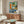 May include: Colorful abstract poster with turntable, geometric shapes in blues, greens, and orange, displayed above walnut credenza in modern living room with white curved chair, brass floor lamp, glass coffee table, and neutral walls